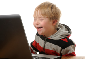 Ung gutt med Down syndrom smiler bredt foran PCen.